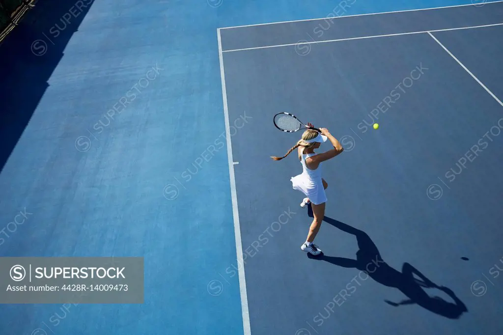 Overhead view young female tennis player playing tennis on sunny blue tennis court