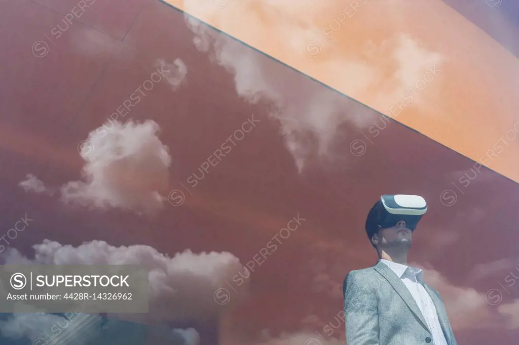 Businessman using virtual reality simulator glasses at window with reflection of clouds