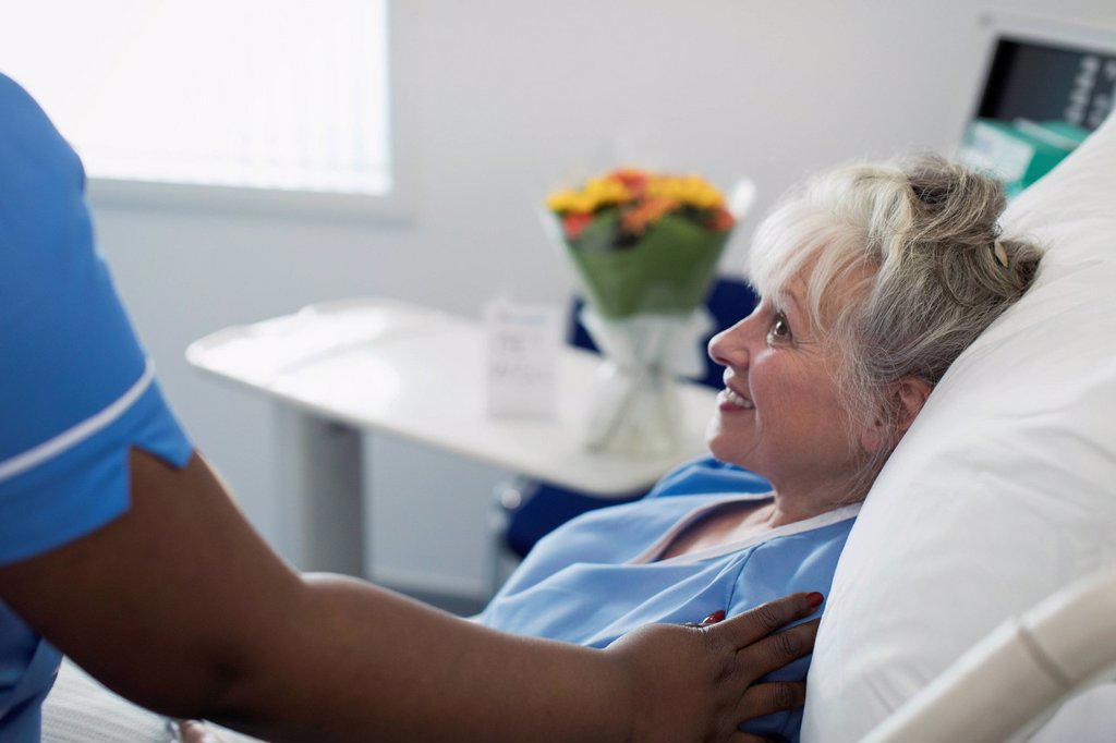 Caring female nurse comforting senior woman resting in hospital bed