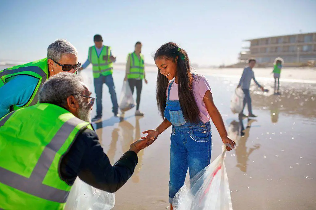 Grandparent and granddaughter volunteers cleaning up litter on sunny wet sand beach