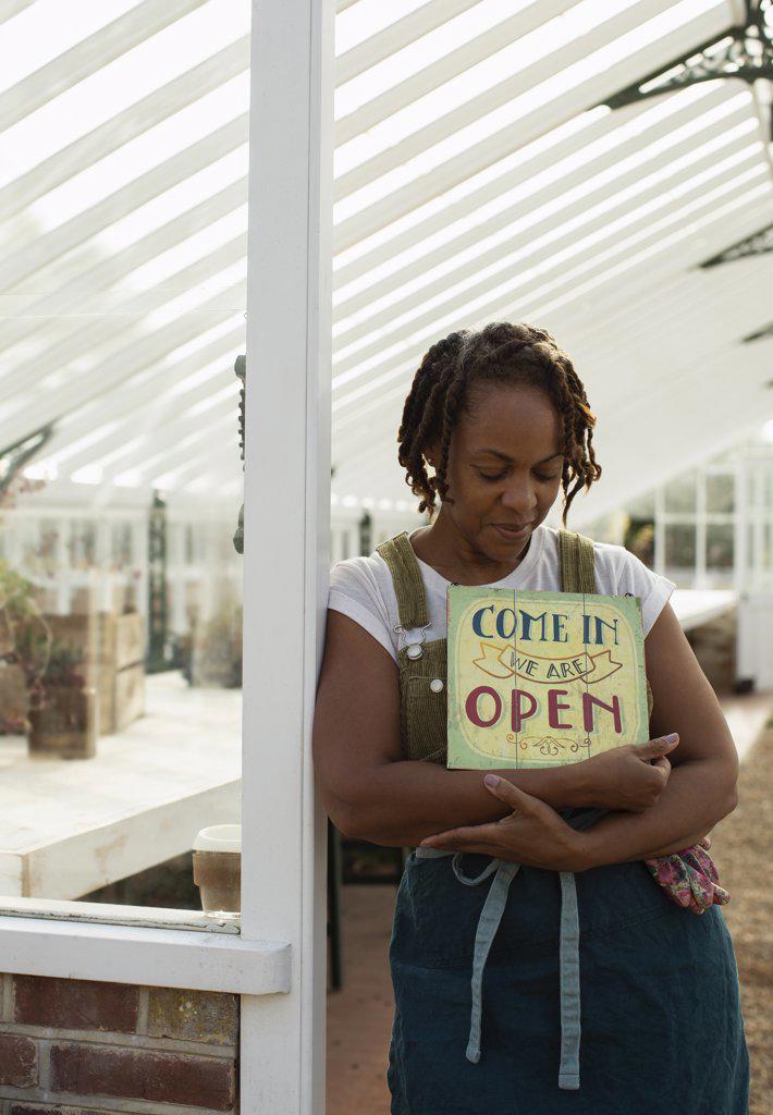 Female plant nursery owner with open sign in greenhouse doorway