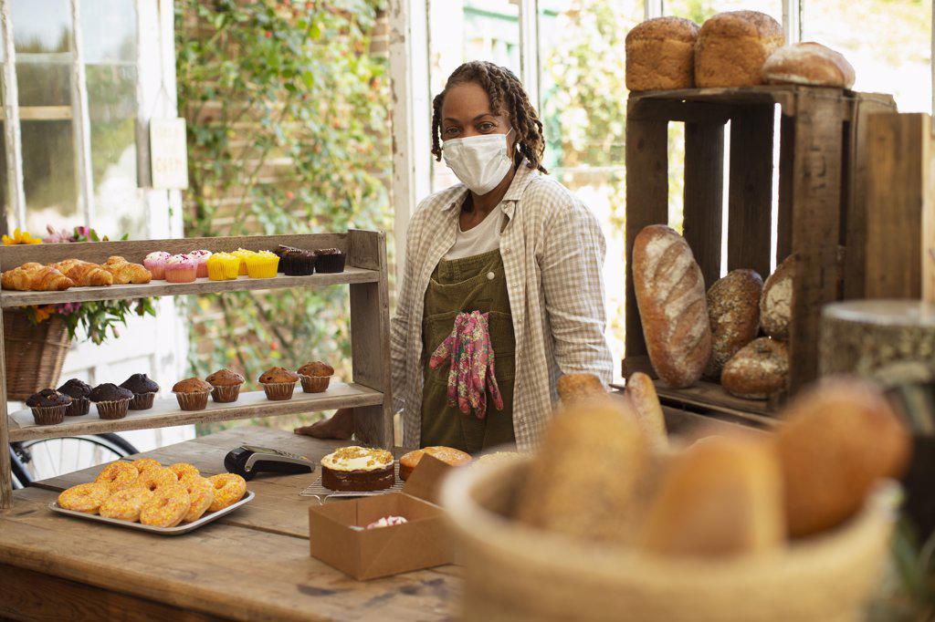 Portrait confident female baker in face mask at pastry display