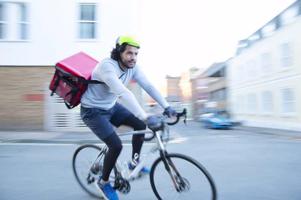 Male bike messenger delivering food on bicycle in urban neighborhood