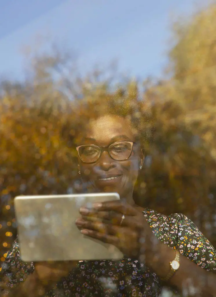 Smiling woman using digital tablet at sunny autumn window