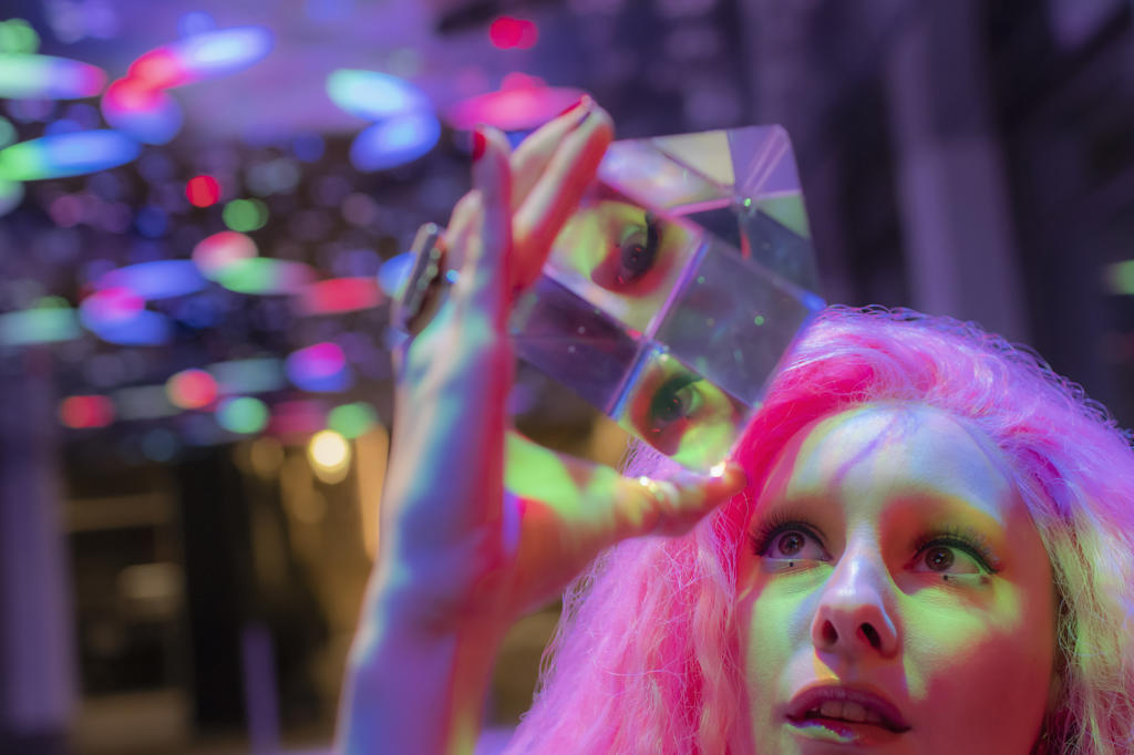 Woman with pink hair looking up at dimensional crystal cube