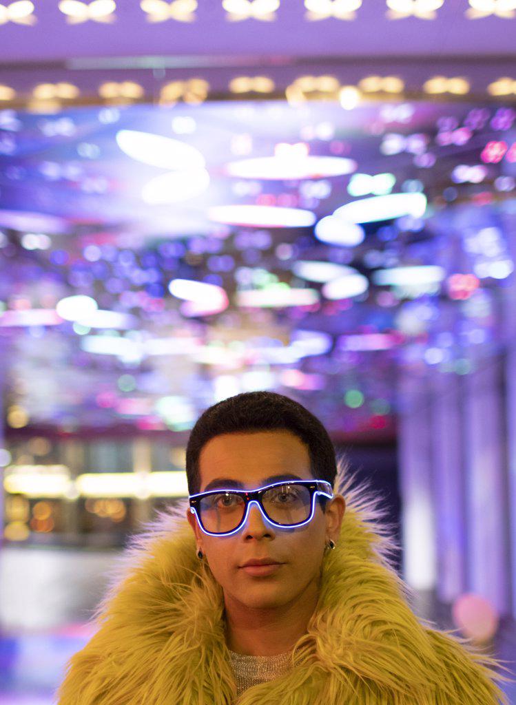 Portrait stylish young man in feather boa and neon glasses