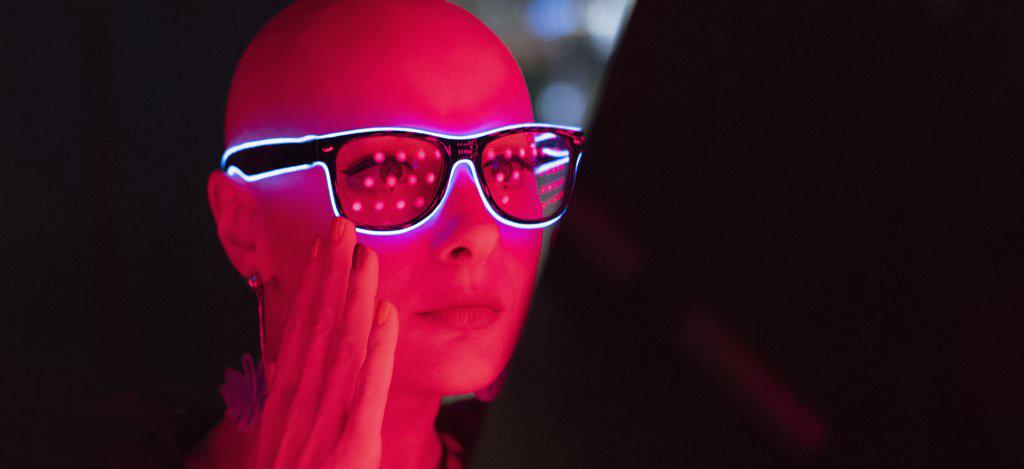 Portrait stylish woman with shaved head in neon glasses in red light