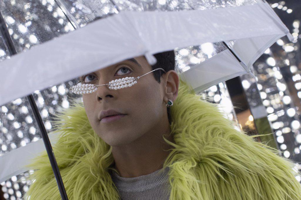 Portrait fashionable young man in feather boa under umbrella