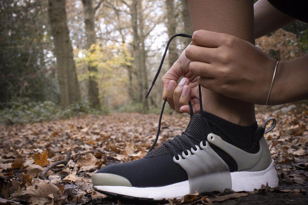 Close up female runner tying shoelace in autumn woods