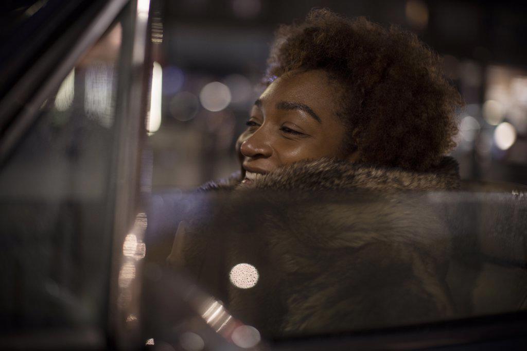 Carefree young woman in fur coat driving convertible at night