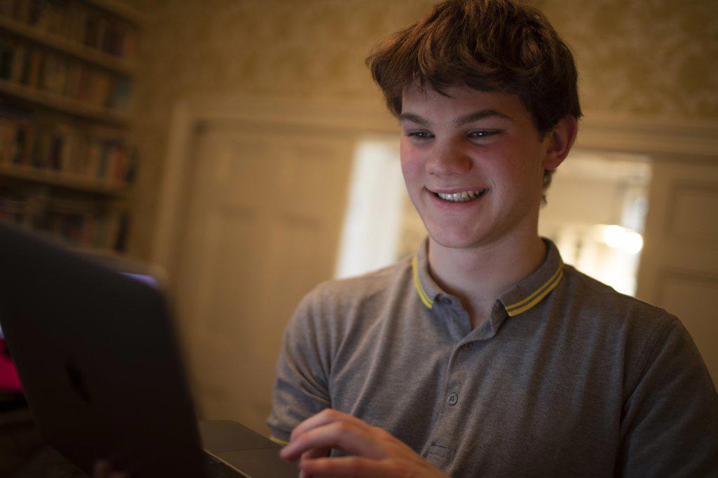Happy teenage boy using laptop at home