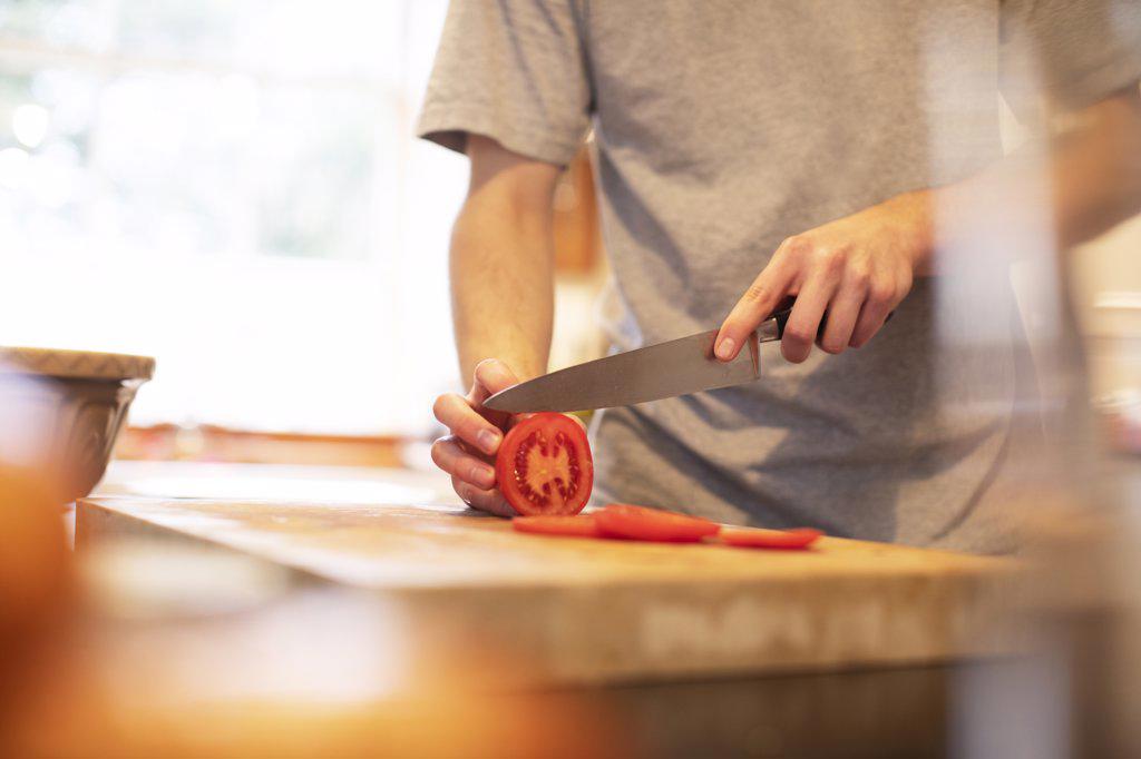 Teenage boy slicing tomato in kitchen