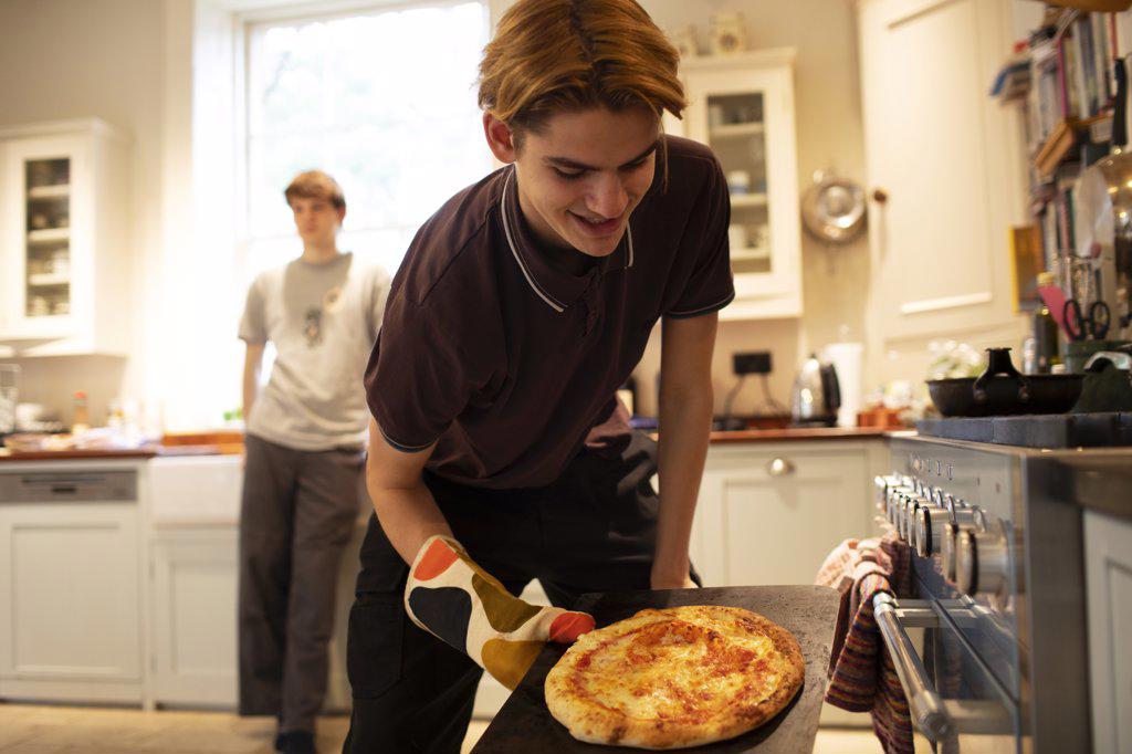 Teenage boy making pizza in kitchen
