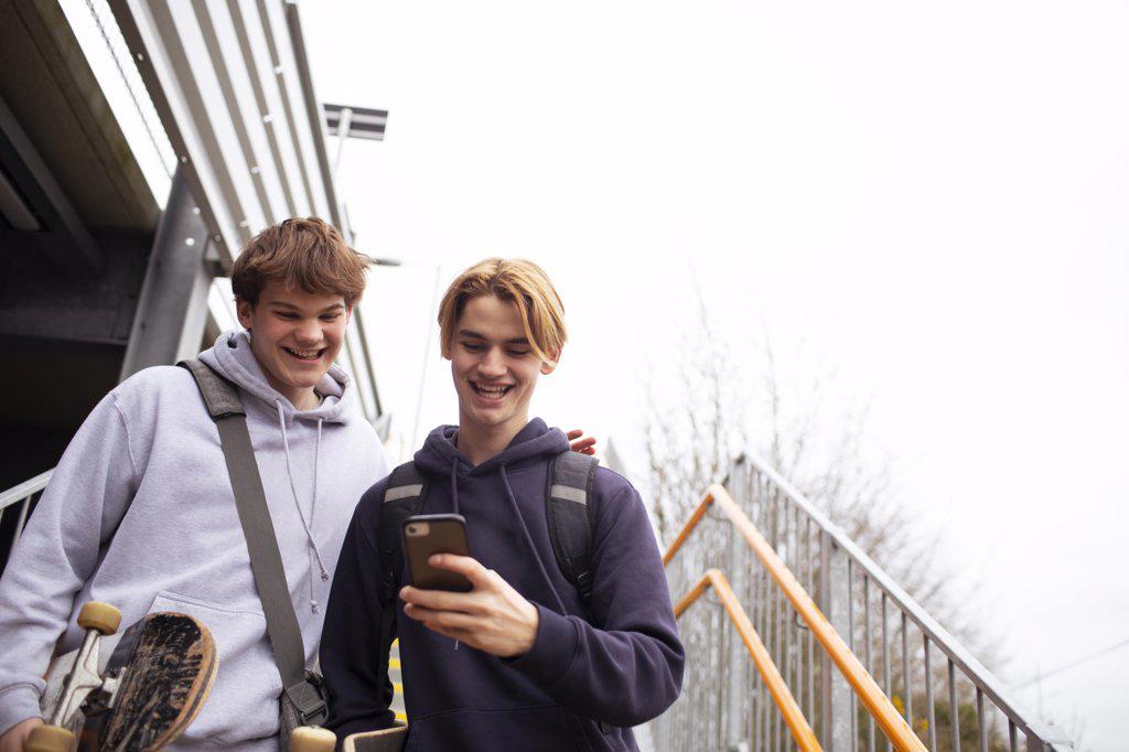 Happy teenage boys using smart phone on steps