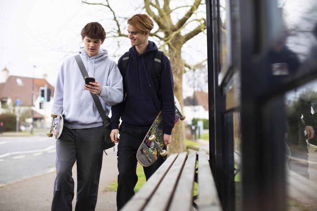 Teenage boys with skateboards and smart phone at bus stop
