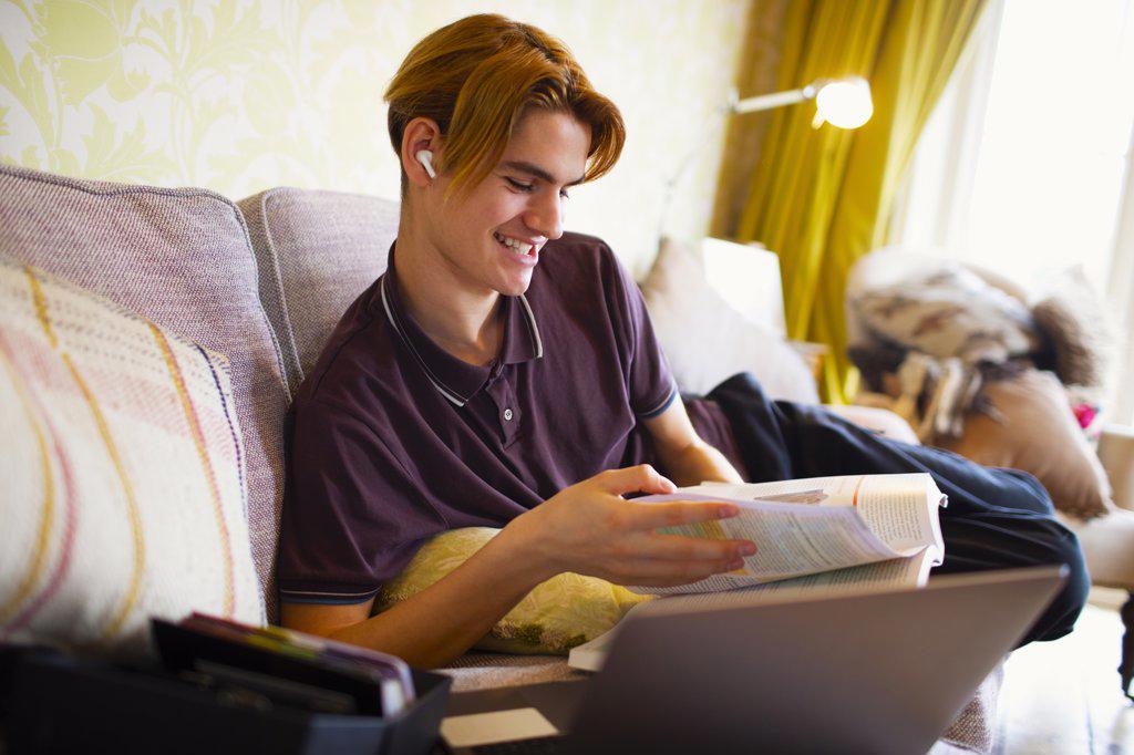 Smiling teenage boy with textbook and laptop studying at home
