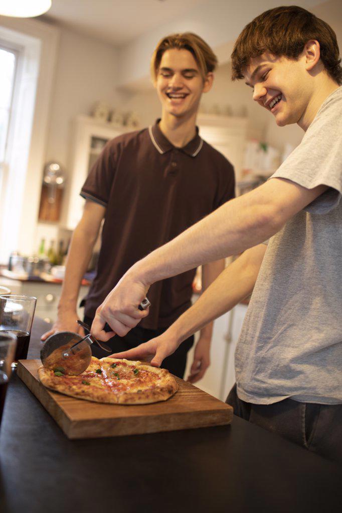 Happy teenage boys slicing fresh pizza in kitchen