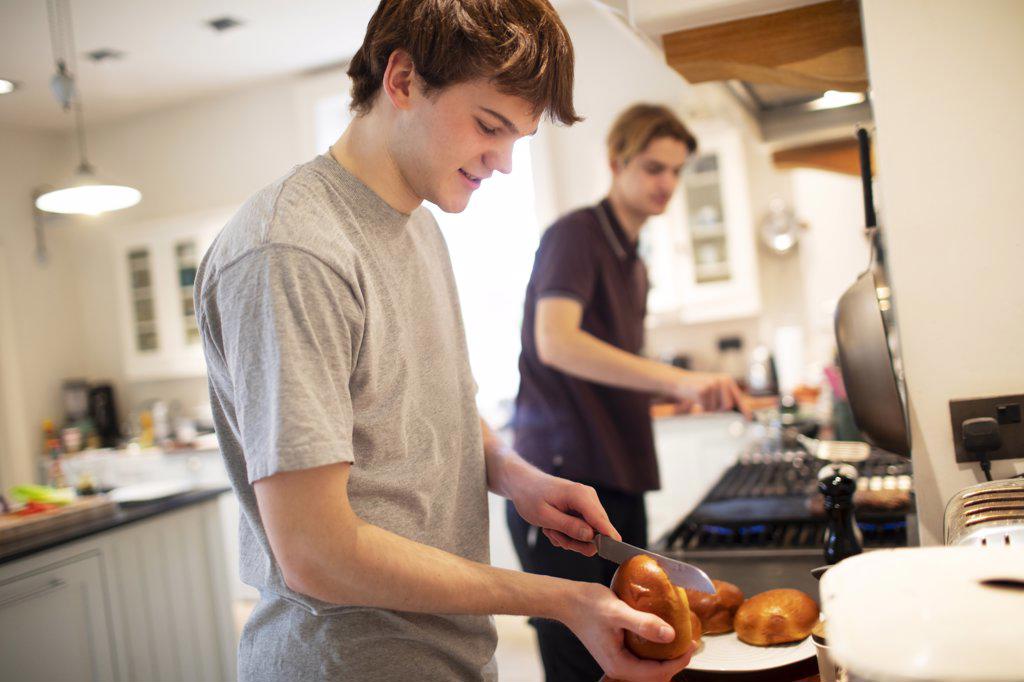 Teenage boy slicing hamburger buns in kitchen