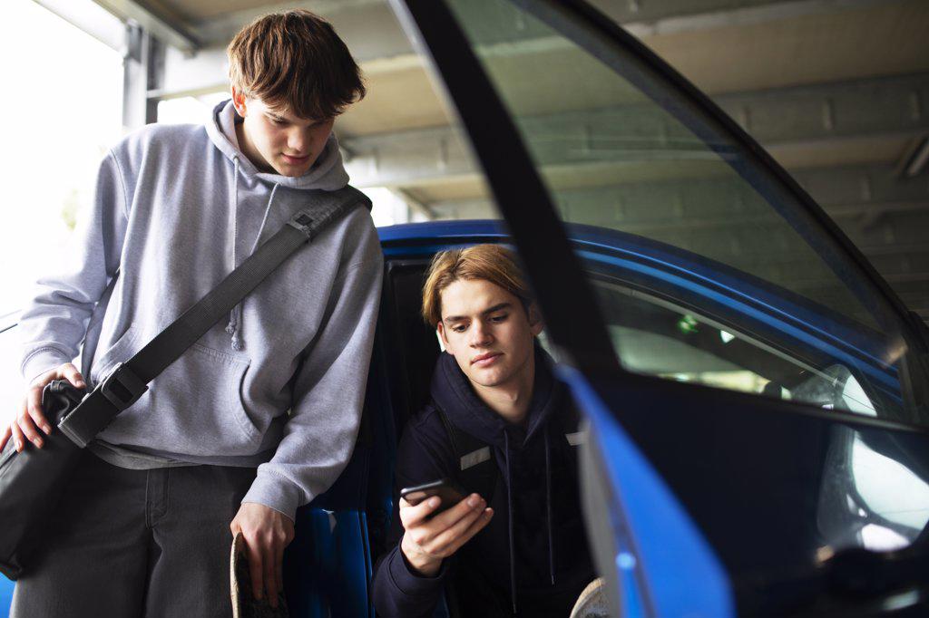 Teenage boys using smart phone at car in parking garage