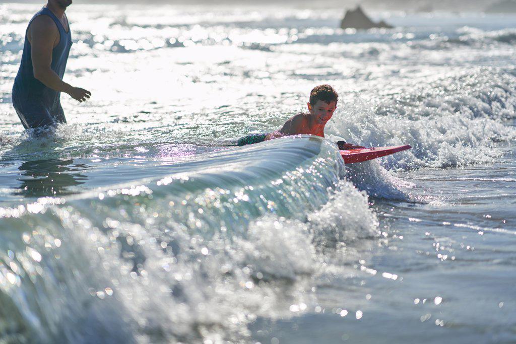 Portrait happy boy body boarding in sunny ocean surf