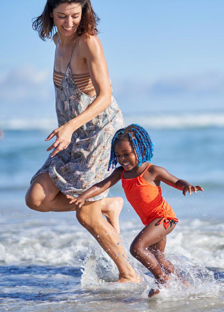 Happy mother and toddler daughter running in sunny ocean surf