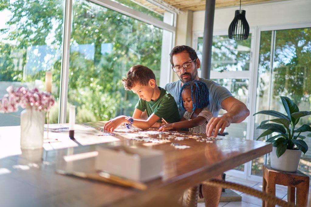 Father and kids assembling jigsaw puzzle at dining table