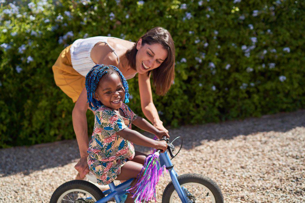 Happy mother helping daughter riding bicycle in sunny driveway