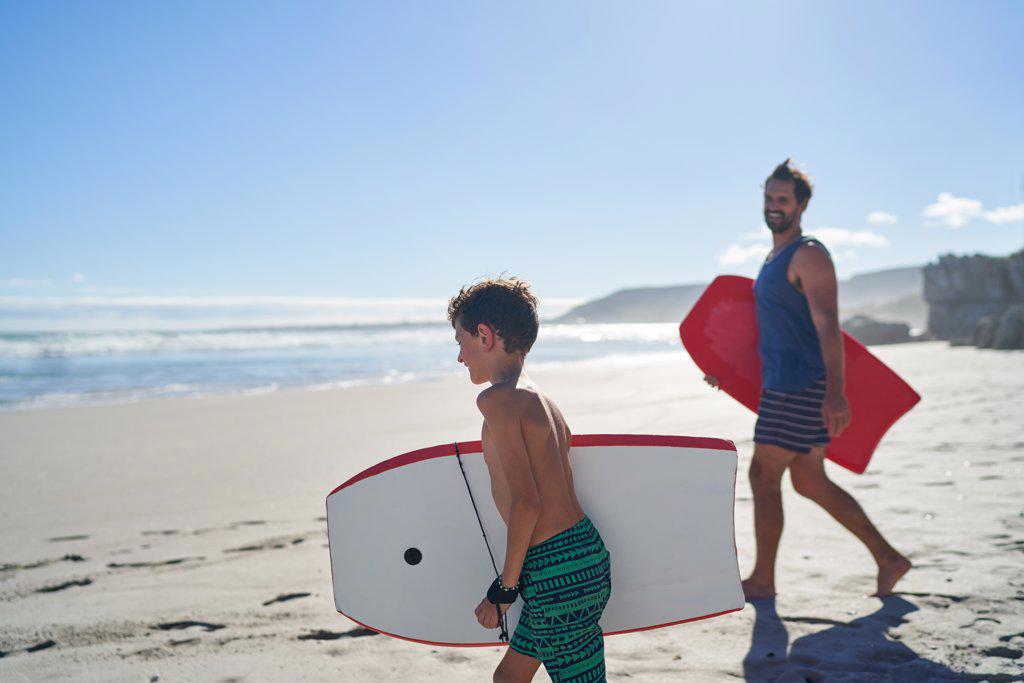 Happy father and son with body boards on sunny summer ocean beach