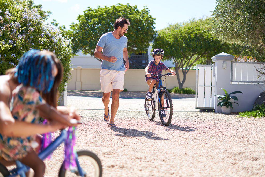 Father and son running and riding bike in sunny driveway