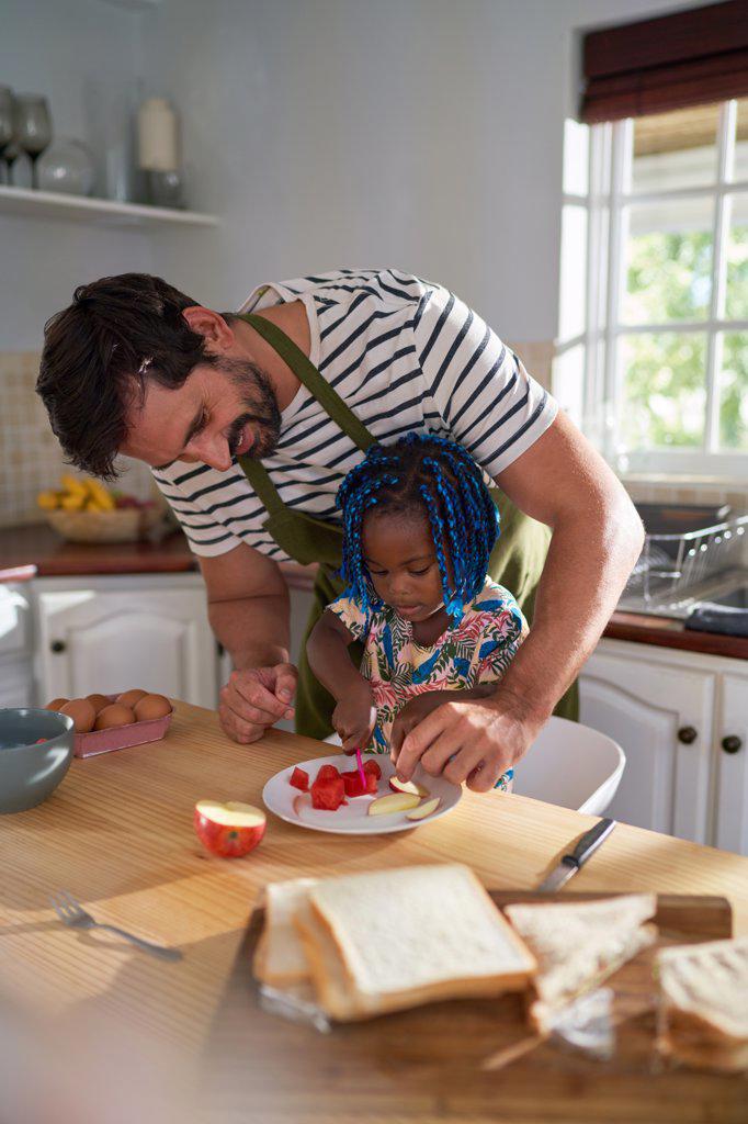Father helping daughter cut fruit in kitchen