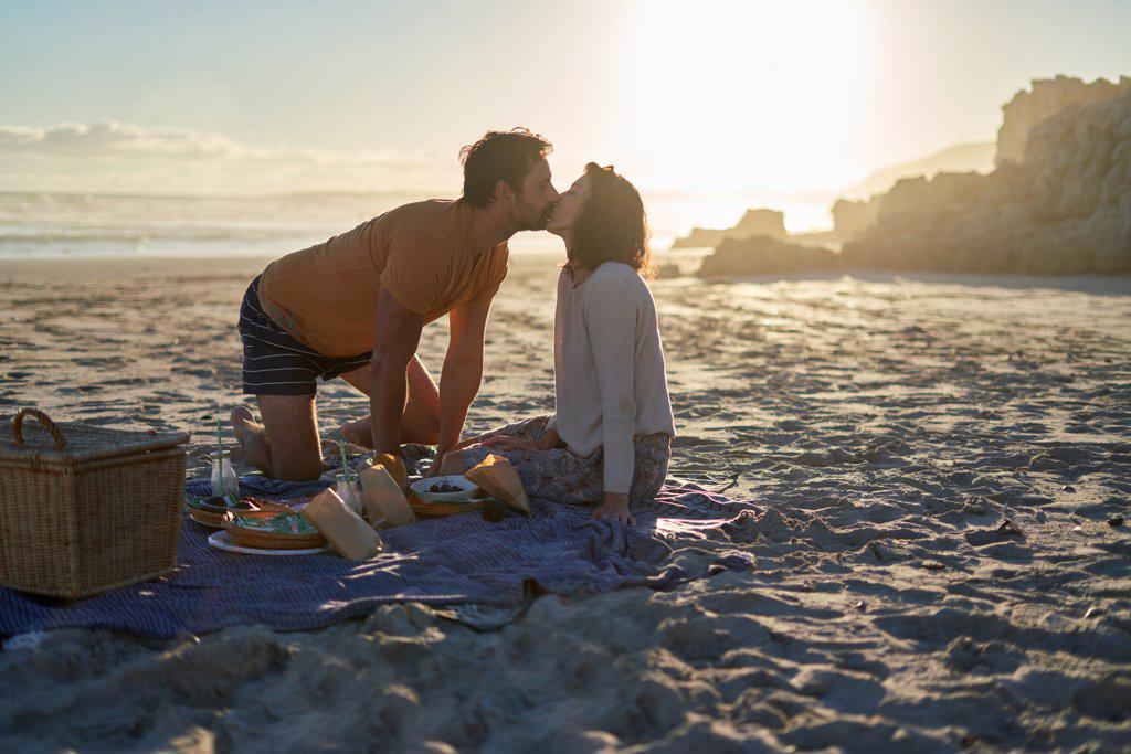 Affectionate couple kissing on picnic blanket on sunny summer beach