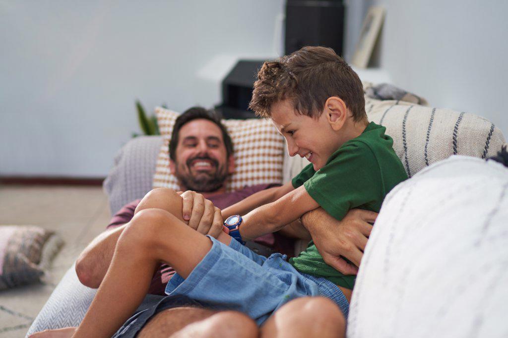 Playful father tickling son on living room sofa