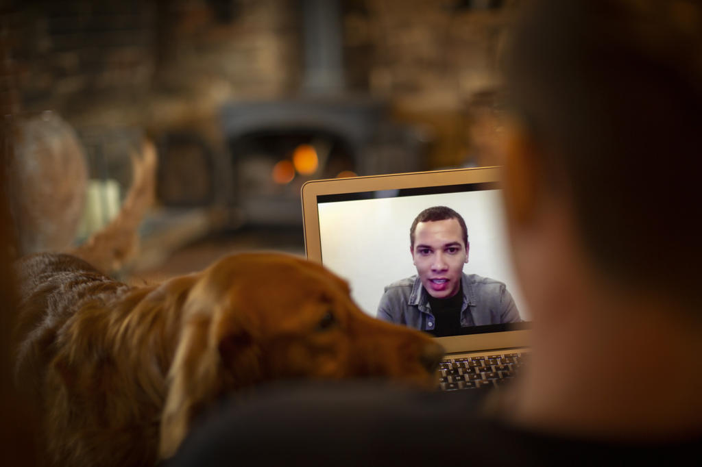Man with dog video chatting with colleague on laptop screen