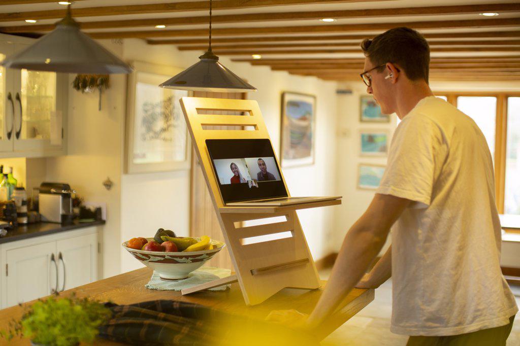 Man video conferencing at laptop stand desk in kitchen