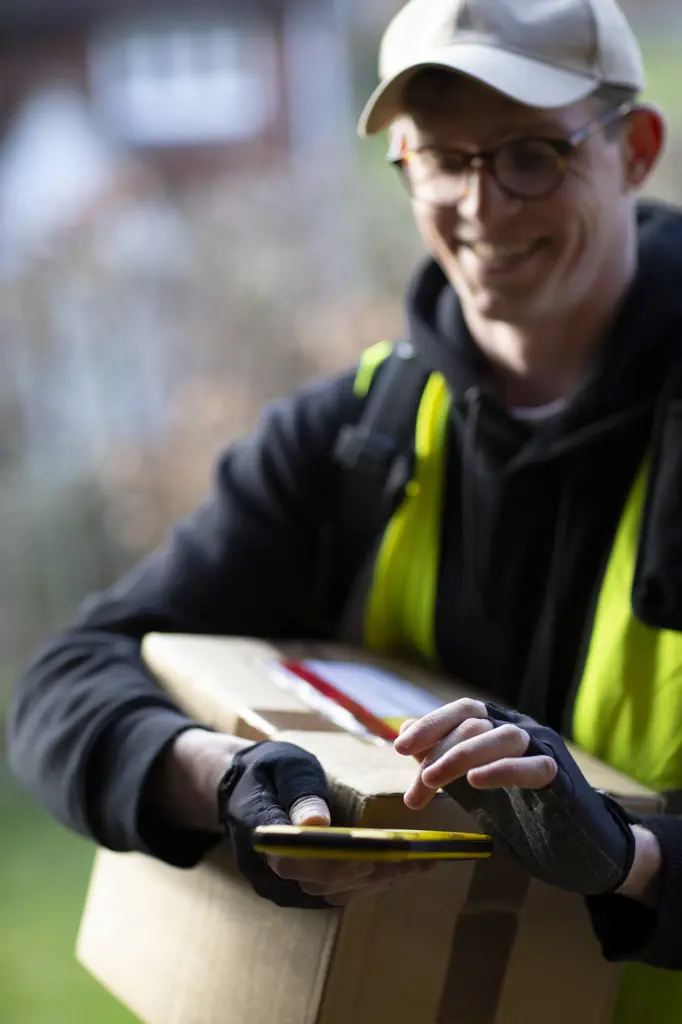Smiling male courier with smart phone delivering package