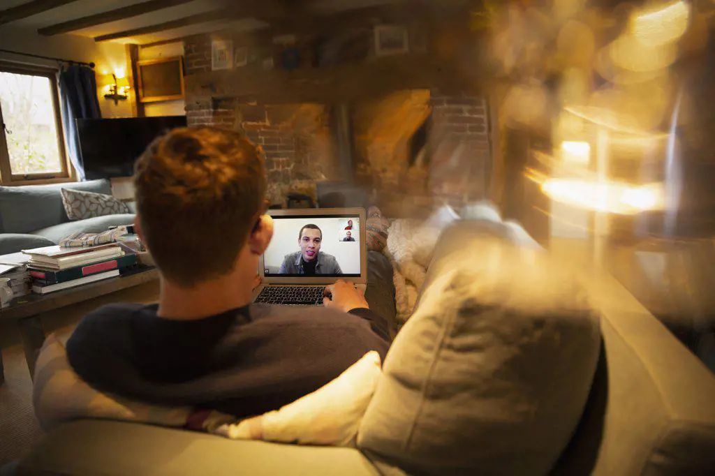 Man video conferencing with colleagues on laptop on sofa