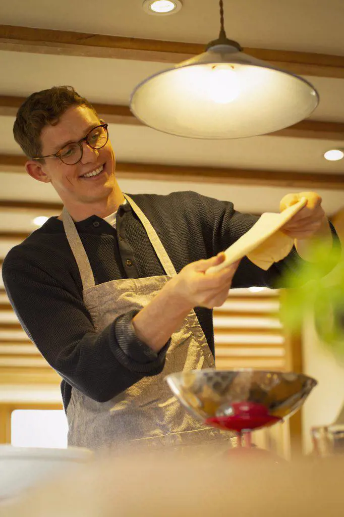 Happy man stretching pizza dough in kitchen