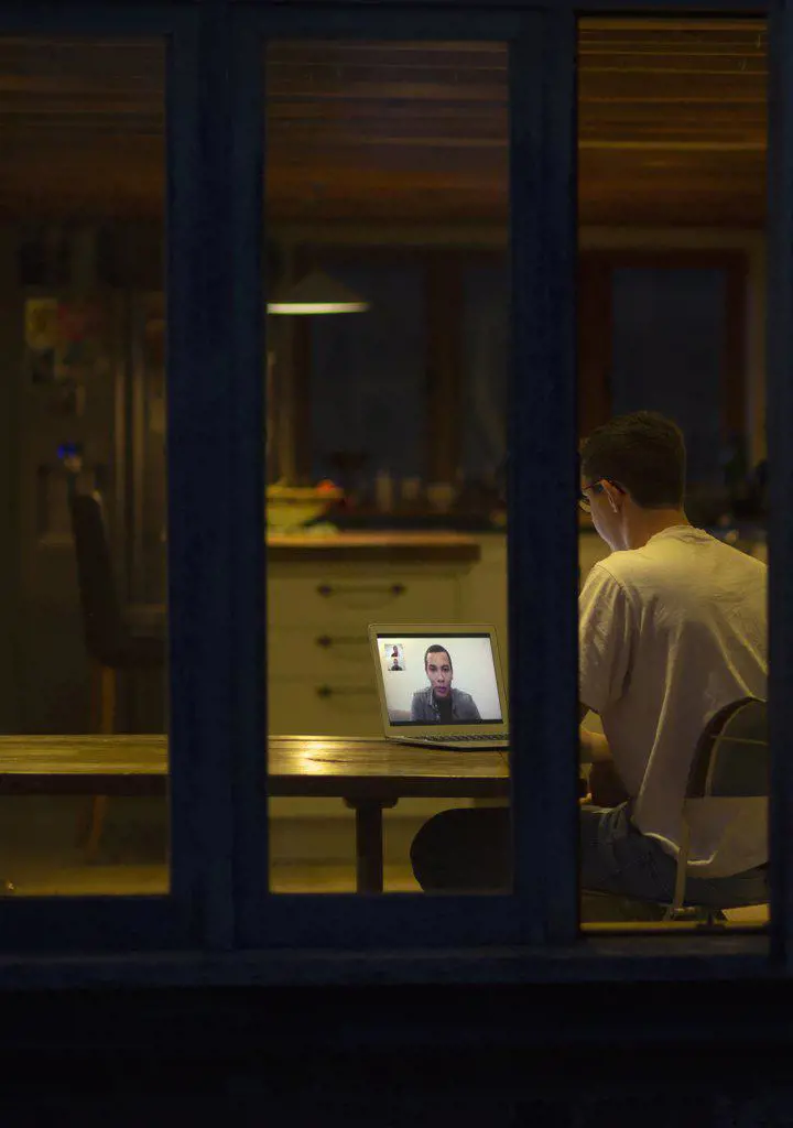 Man working late video conferencing with colleagues in dark kitchen