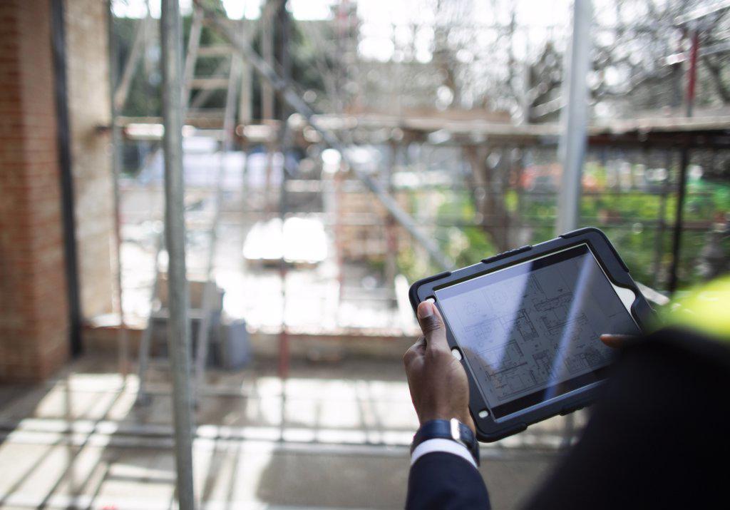 Engineer looking at blueprints on digital tablet at construction site