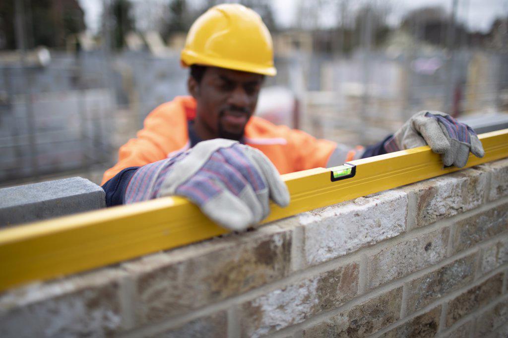 Male construction worker using level tool on brick wall