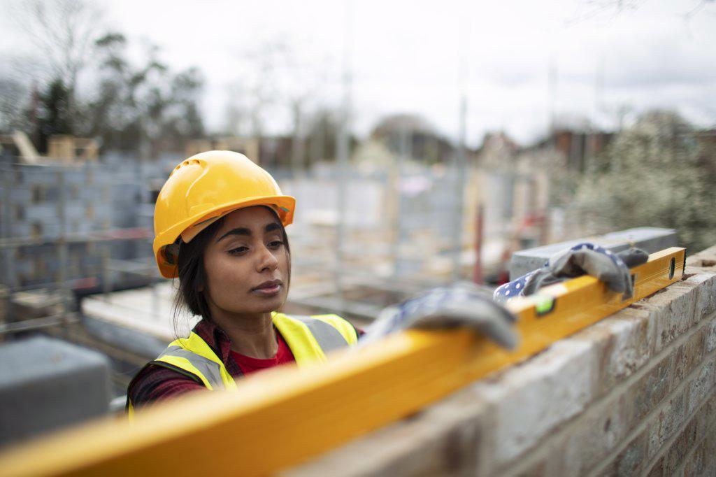 Female construction worker using level tool on brick wall