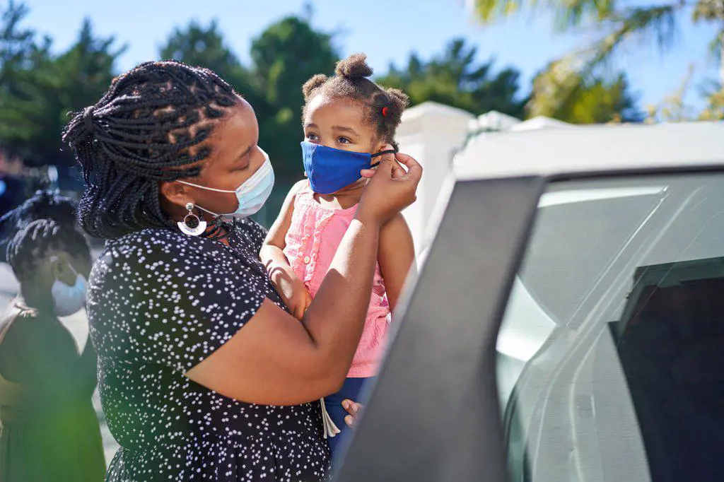Mother helping daughter with face mask outside car