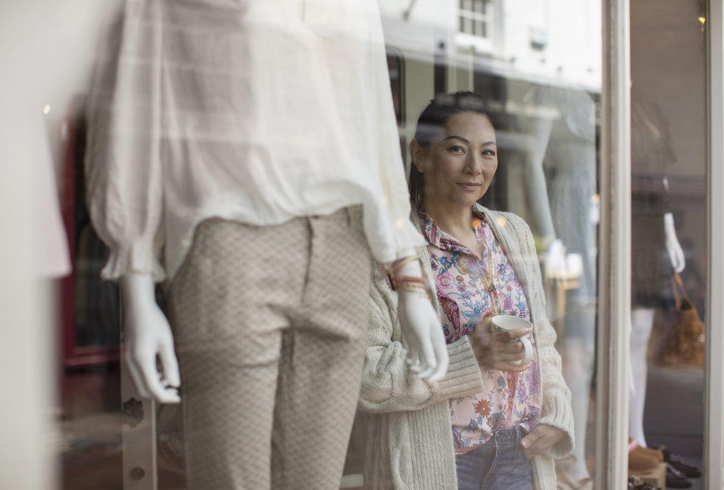 Portrait confident female shop owner drinking tea at boutique window