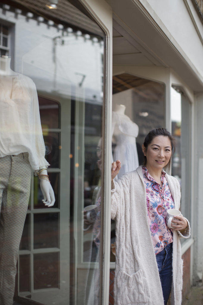 Portrait confident female shop owner drinking coffee outside boutique
