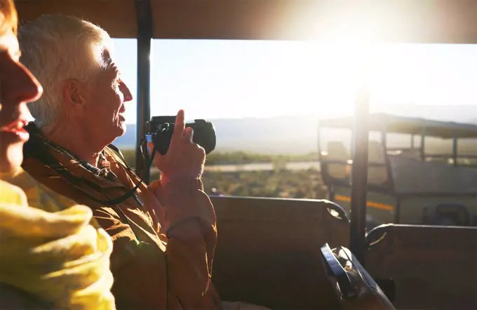 Senior couple with digital camera riding in safari off-road vehicle