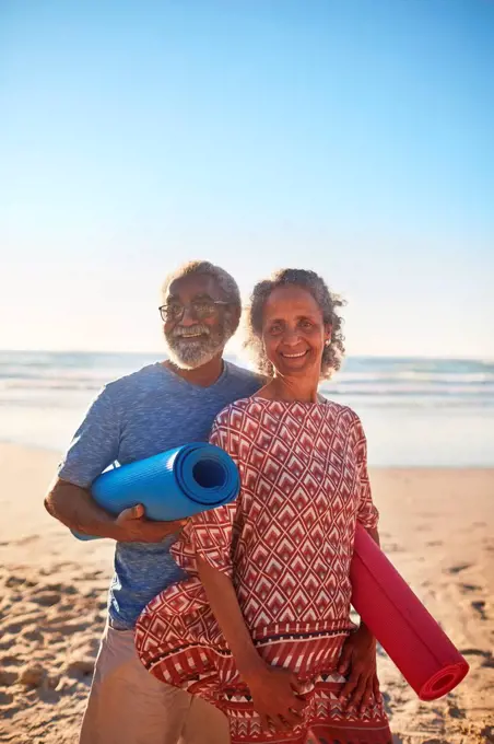 Portrait happy senior couple with yoga mats on sunny beach