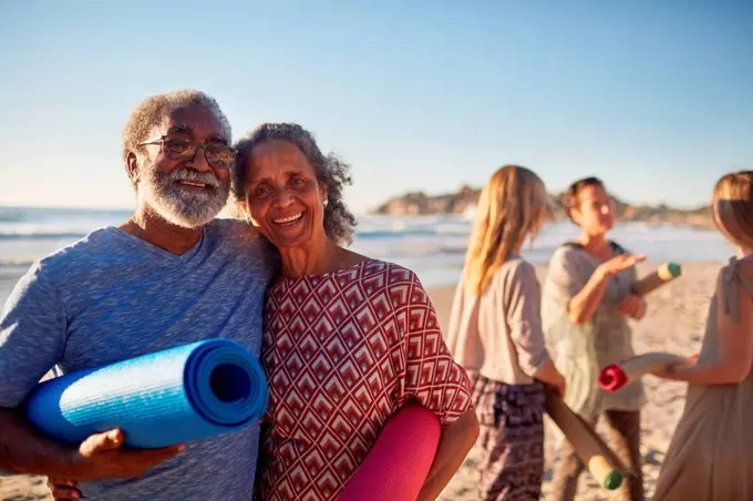 Portrait happy senior couple with yoga mats on sunny beach during yoga retreat