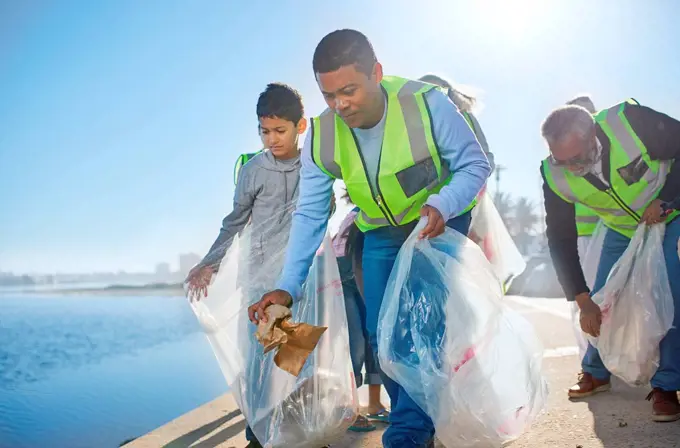Multi-generation family men volunteering, picking up litter on waterfront pier