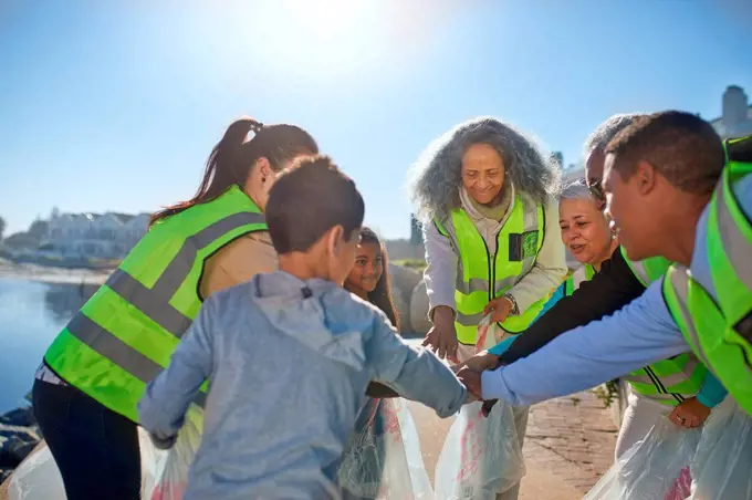 Volunteers forming huddle, cleaning up litter on sunny beach
