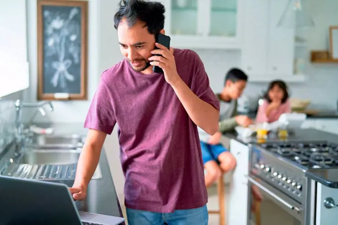 Man working at laptop in kitchen with kids